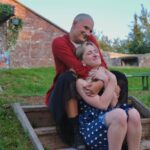 The Cambridge Battery on a beautiful clear day. In the Centre of the Image, Zach who plays The Nurse and Jade who plays Juliet sit together in a loving embrace. The Nurse is sweetly hugging Juliet. Both people look beautiful and perfectly content.