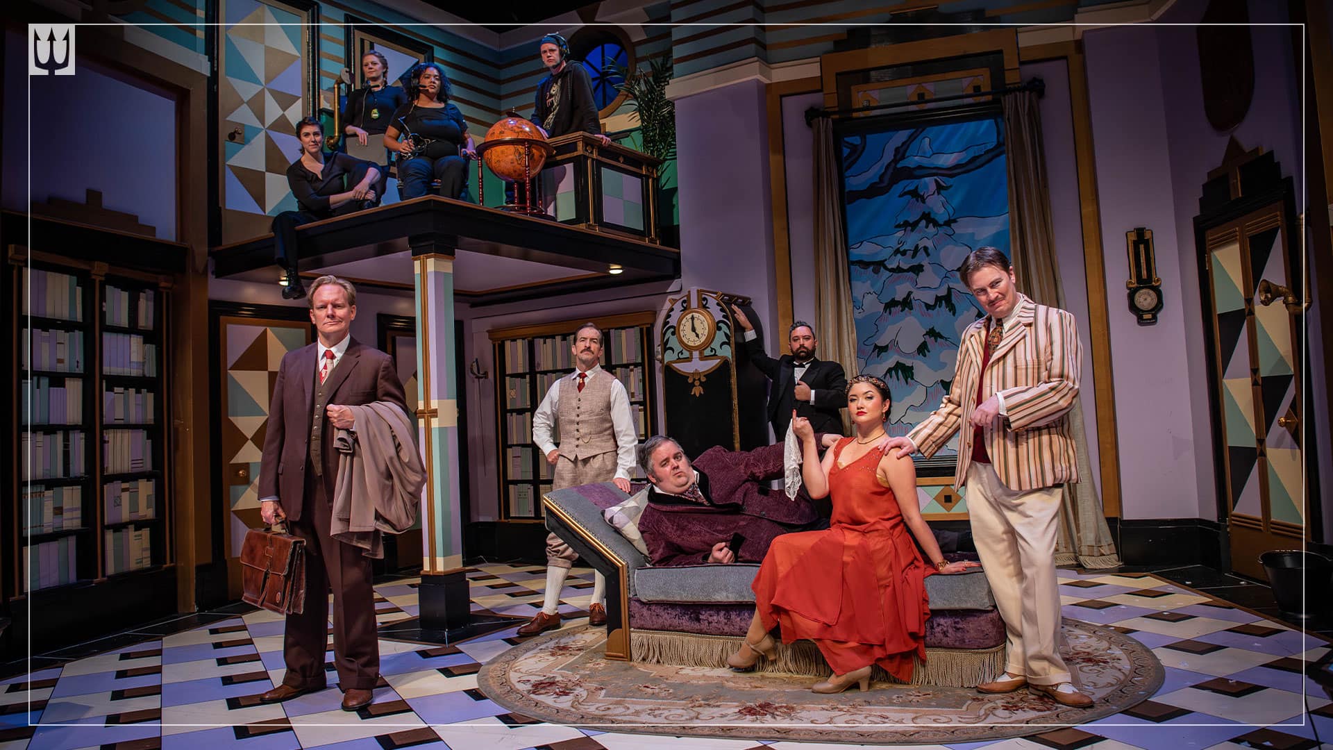 A "Vanity Fair" style shot of six actors on a huge theatre set in 1920s costumes. On a platform above them are four crew members. The crew members do not look excited about the play.