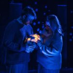 ID a man and a woman hold a bundle of lights, wrapped like a baby, washed and dark and moody blue lights