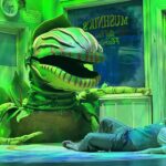 A very green photograph of a very large flytrap plant with its mouth open menacing a very small nerdy human man named Seymour, who is lying on the floor trying to get away.