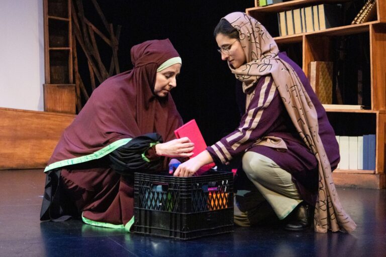 Two Iraqi women are loading up a milk crate with library books. They look very serious about their work.