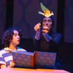 A young Iraqi boy wearing a striped shirt looks in awe as a yellow and green bird puppet flies out of his open book.