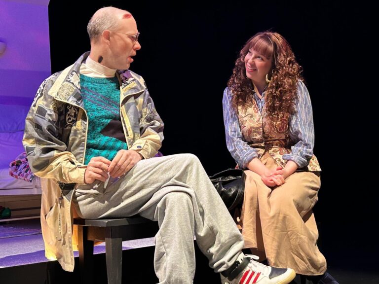 A gay man dying from AIDS, he has lesions on his face and wears baggy clothes, he sits facing his sister, a healthier looking woman in her 30s with brown, long, curly hair.